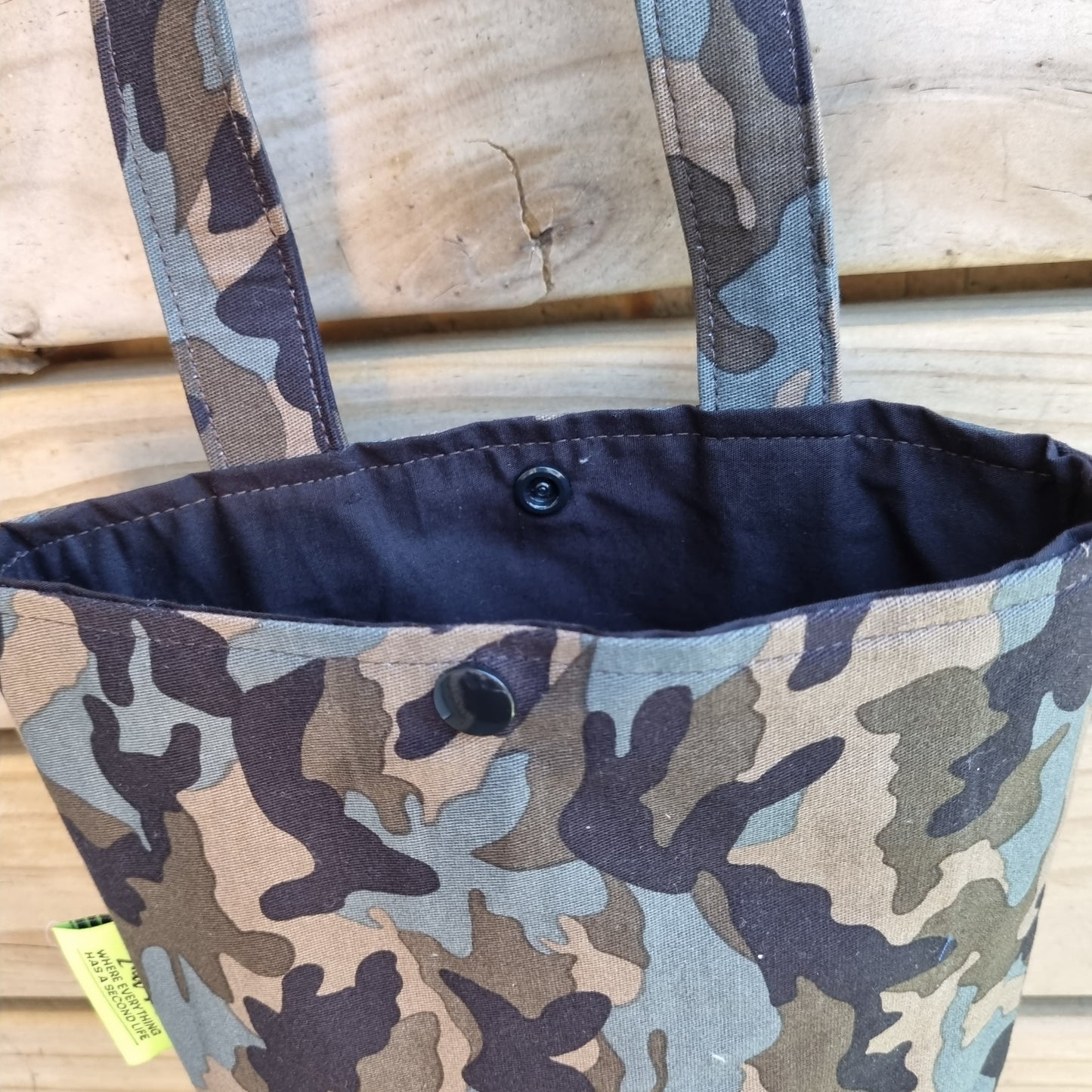 Camouflage-patterned bag with a button and strap on a wooden surface