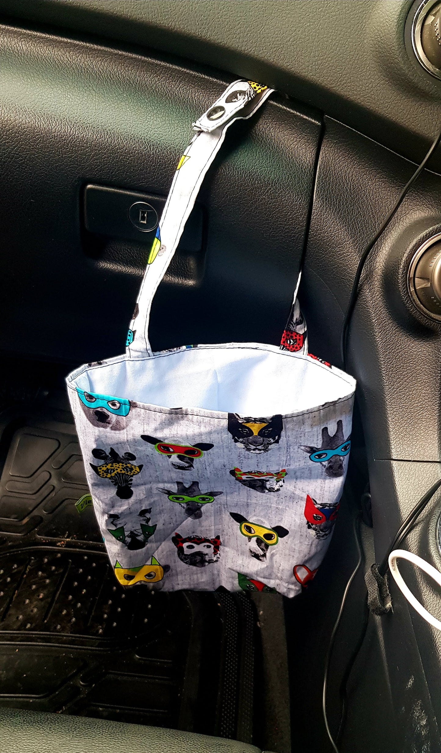Fabric tidy bag with superhero designs hanging from a car's dashboard.