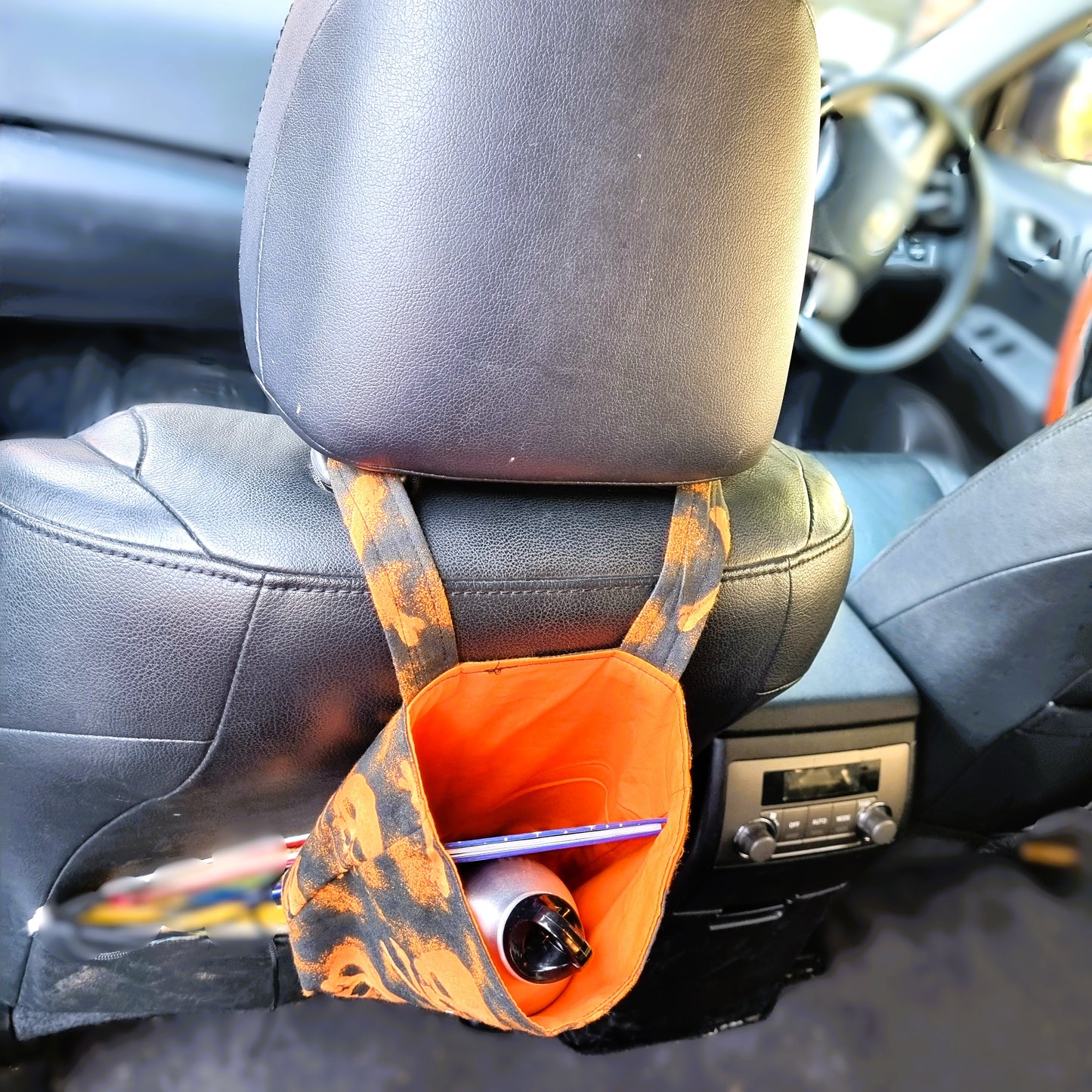 Car headrest organizer with orange pouch holding a pen and bottle inside a car.