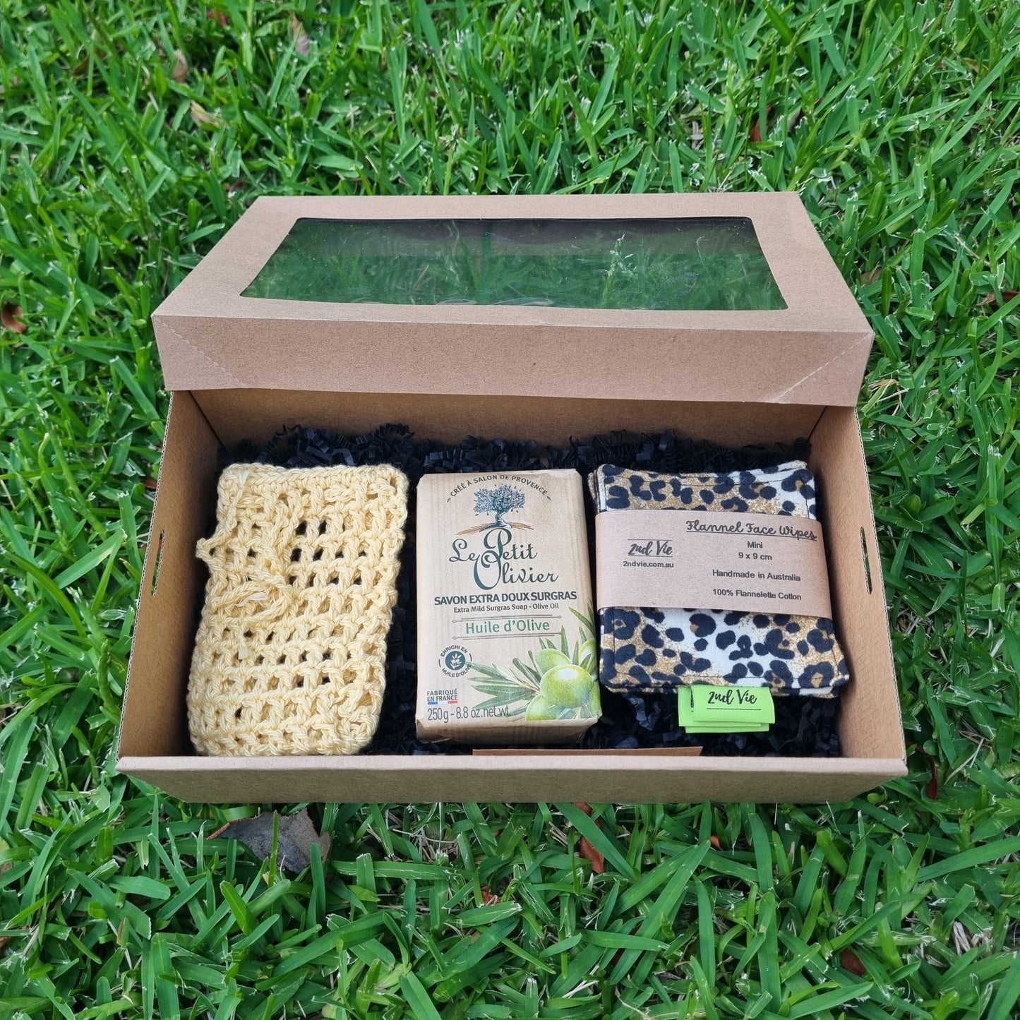 Box of soap bars and a loofah on grass