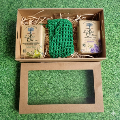 Gift set with soaps and a scrubber in a brown box on a green grass-like background