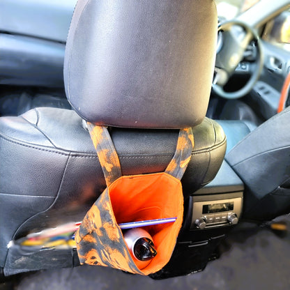 Car headrest organizer with orange pouch holding a pen and bottle inside a car.