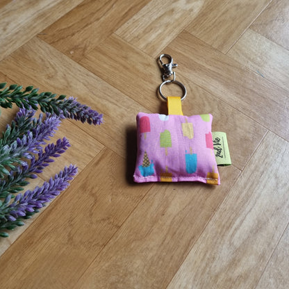 Small pink fabric pouch with colorful icecream on a wooden floor with lavender flowers.