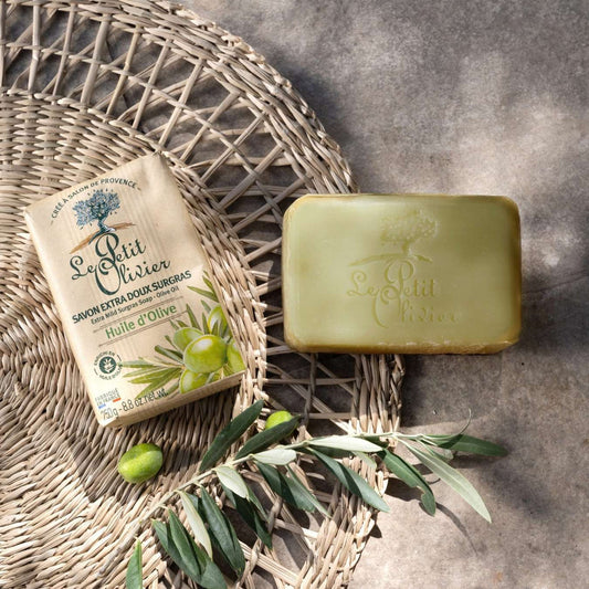 Olive Oil Bar of soap and packaging with olive leaf on a woven mat and stone surface