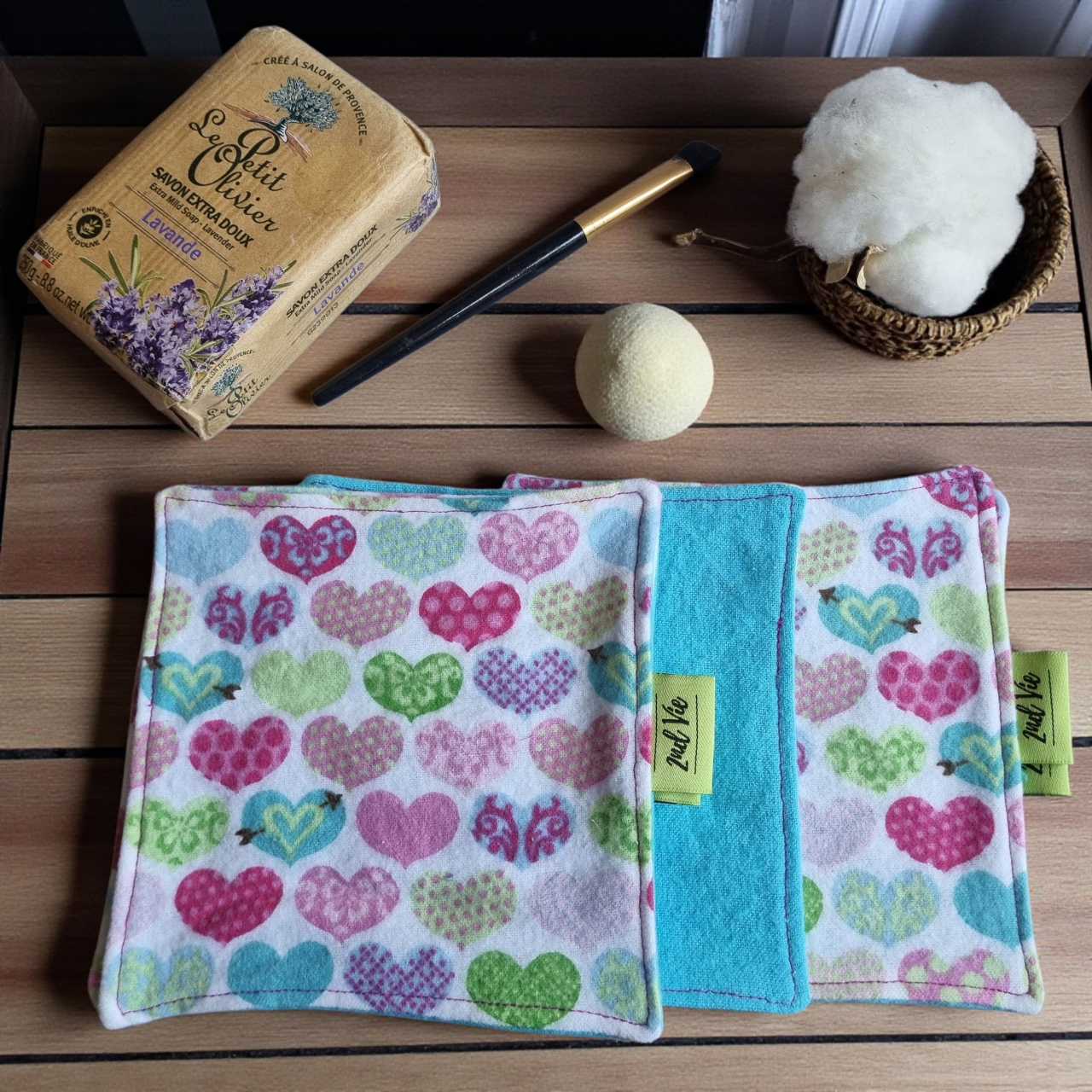 Sustainable makeup remover pads with cute multi-coloured heart pattern in pink, blue, and green, photographed with natural soap and cotton