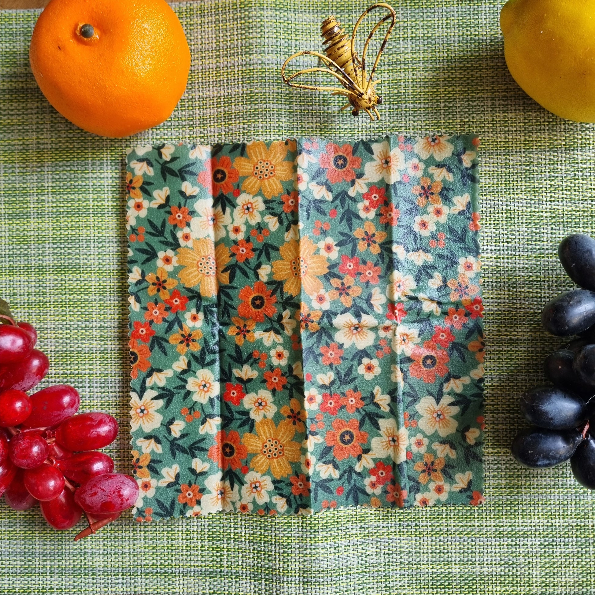 Floral-patterned food wraps on a green surface with fruits and grapes.