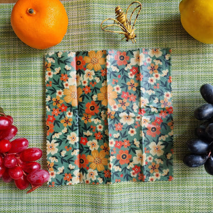 Floral-patterned food wraps on a green surface with fruits and grapes.