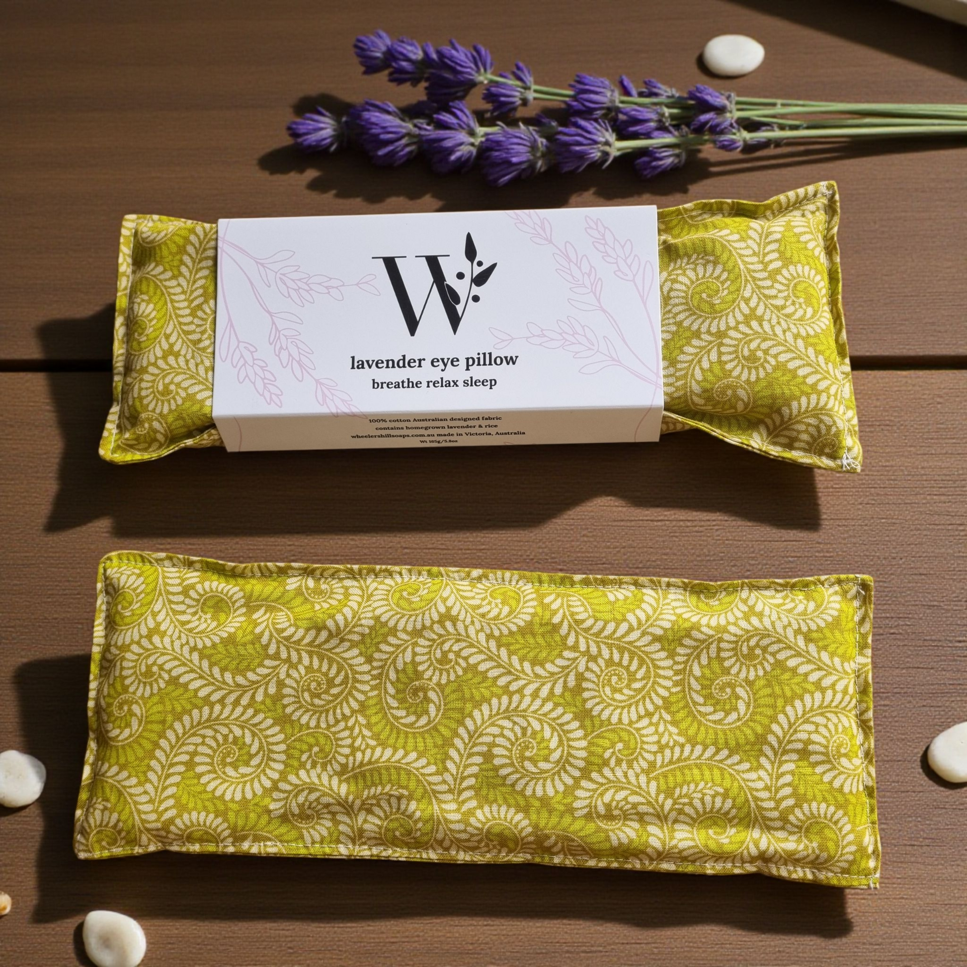 Two fern pattern  lavender eye pillows  with a packaging card on a wooden surface.