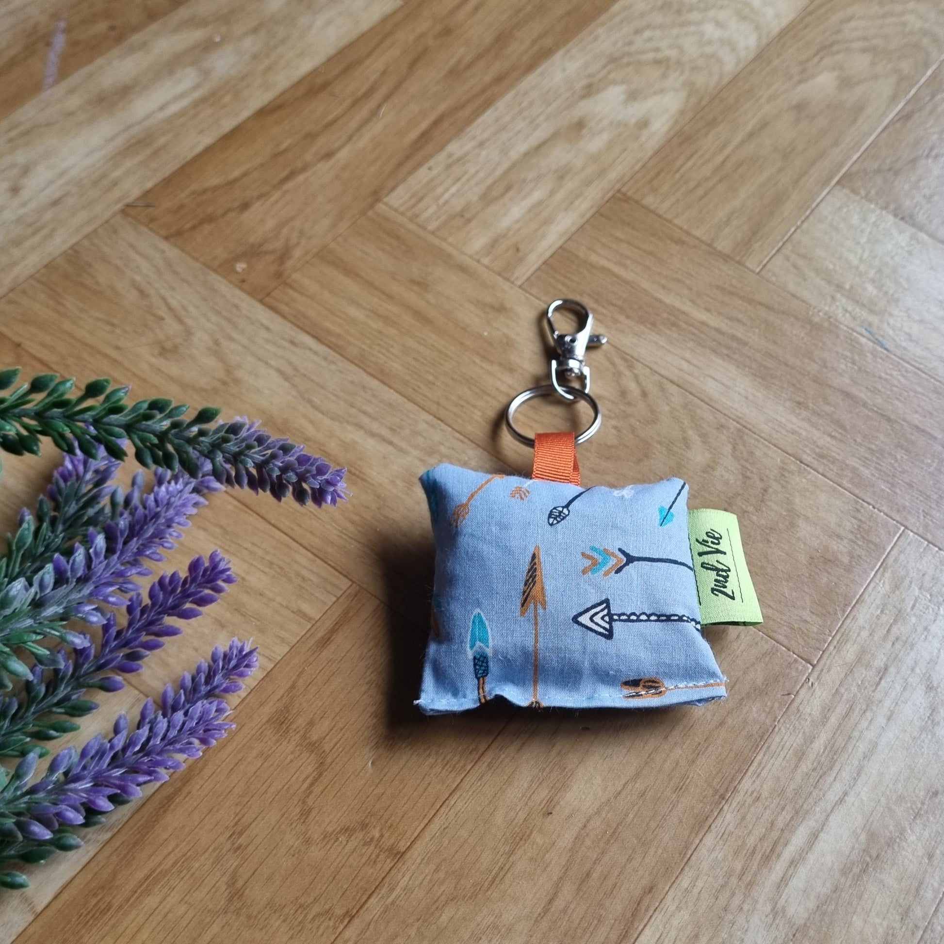 Small blue fabric pouch with keychain on a wooden floor with lavender flowers.