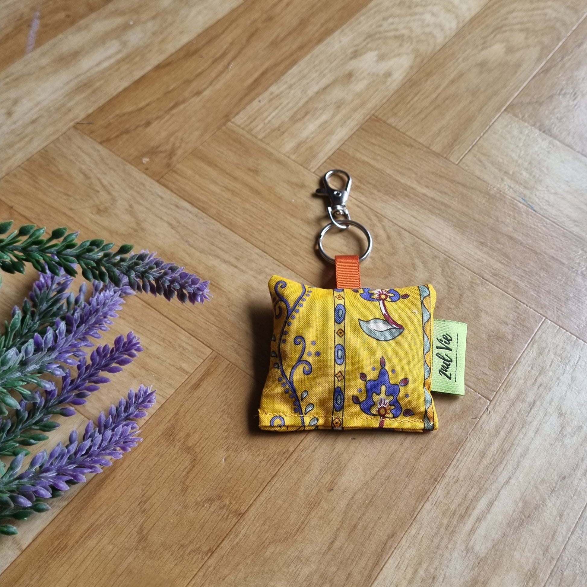 Yellow fabric keychain with a decorative design on a wooden floor.