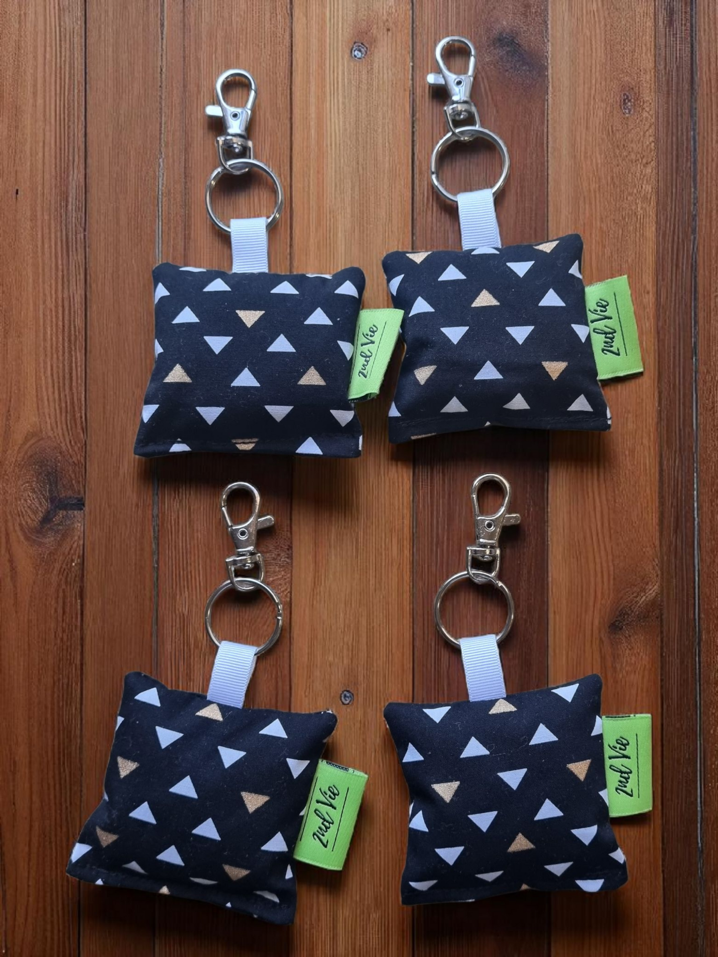 Four black fabric keychains with white triangle patterns on a wooden surface